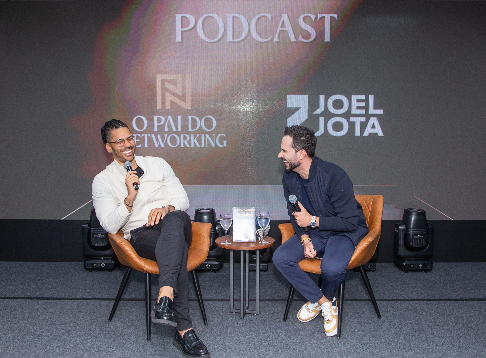 Conversa em palco com letreiro do podcast O Pai do Networking e Joel Jota